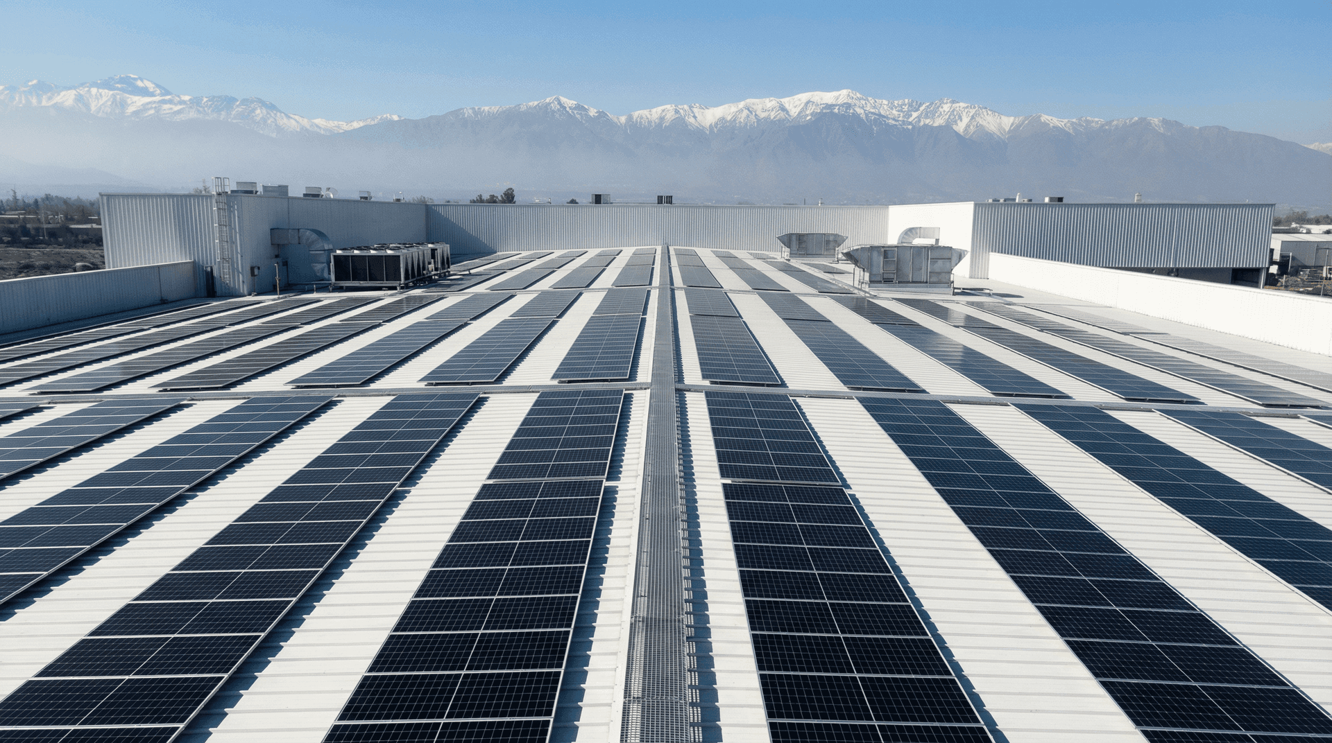 Paneles solares sobre la cubierta de una nave industrial, con la cordillera de los Andes de fondo